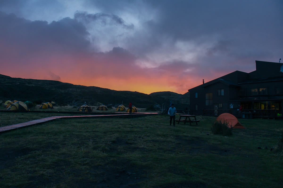 Refugio Paine Grande in Torres del Paine at dusk, with tents on the grass and the hut windows lit